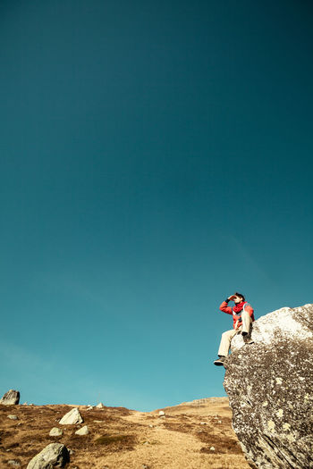 Man on rock against clear blue sky