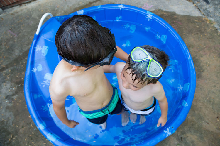 High angle view of shirtless siblings standing in wading pool