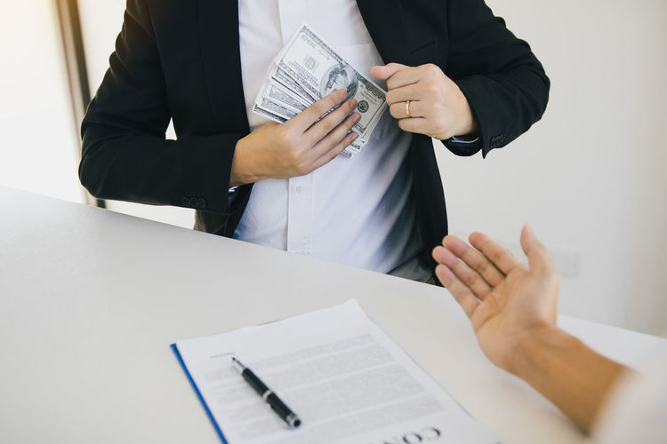 Cropped hands of business person keeping bribe in pocket by man gesturing on table