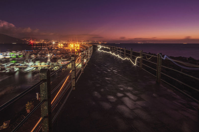 Illuminated bridge over sea against sky at night