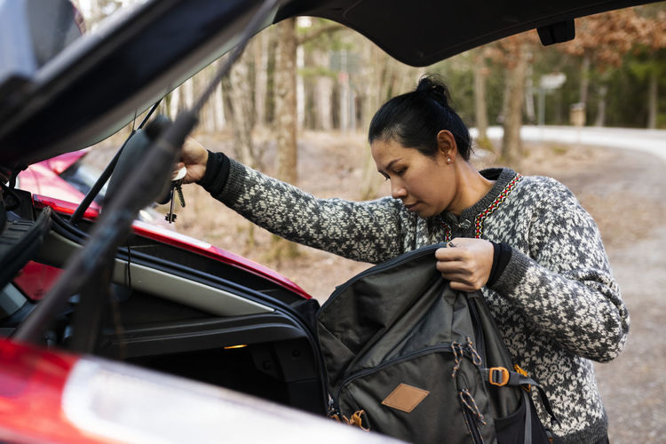 Woman putting backpack in car trunk