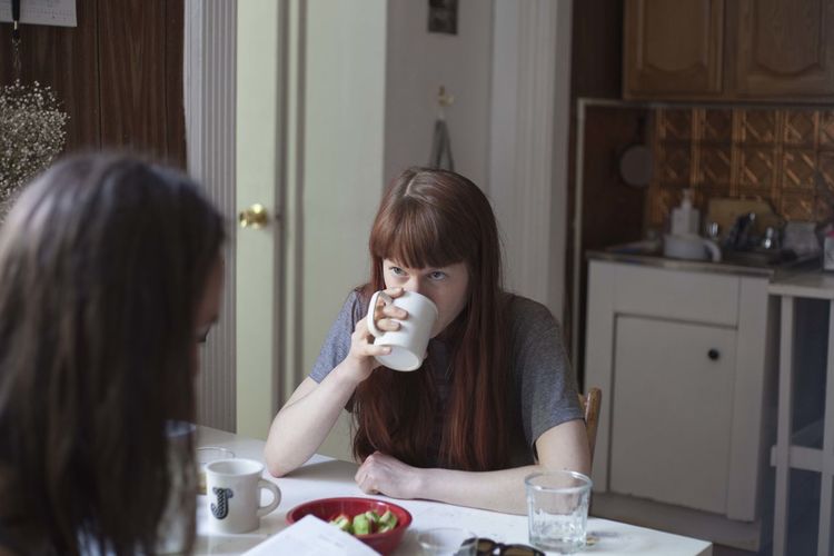 Young woman looking at her boyfriend while drinking coffee