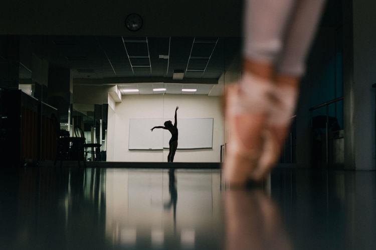 Low section of woman practicing ballet with reflection in mirror at dance studio