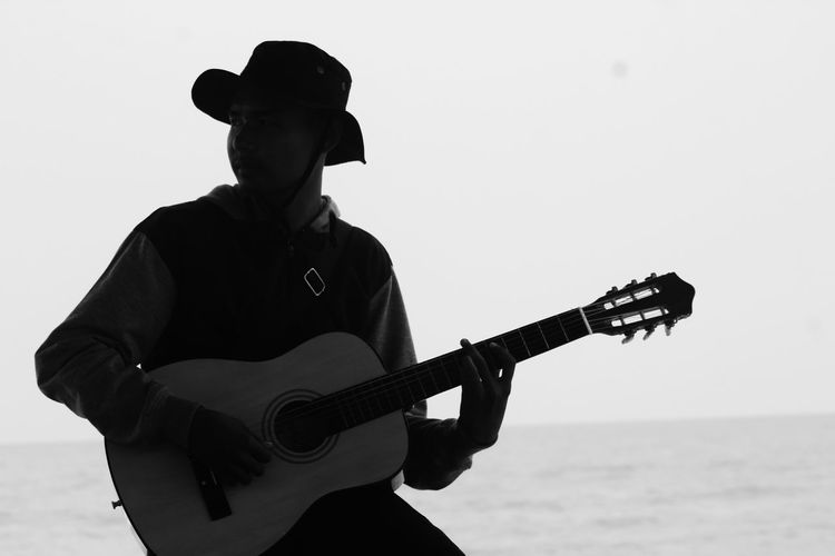 Man playing guitar at sea against sky