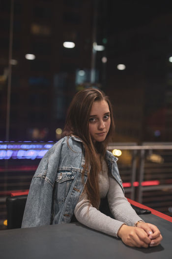 Portrait of beautiful young woman sitting on table at night