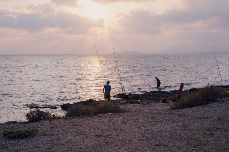 People fishing at beach against sky