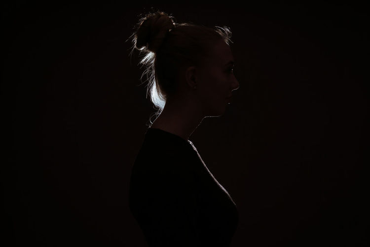 Portrait of young woman looking away against black background