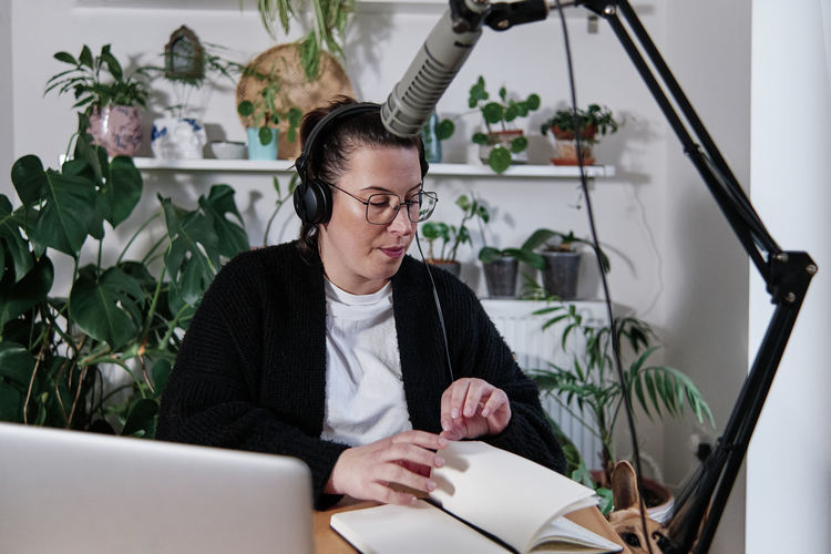 Woman doing podcast session while sitting against plant at home