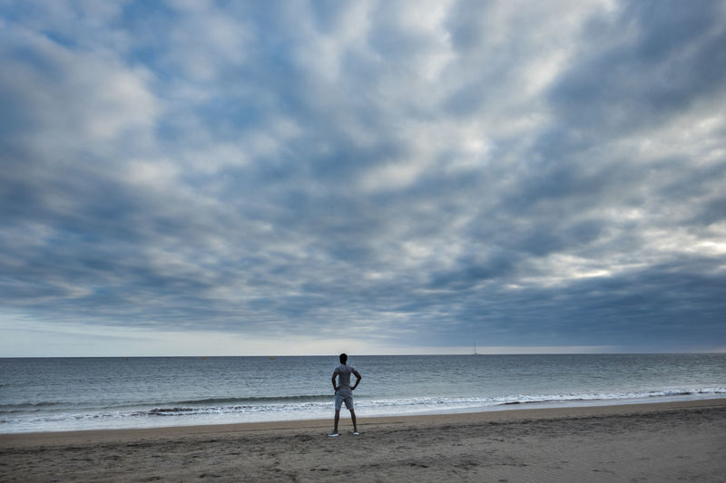 Man standing at beach against cloudy sky