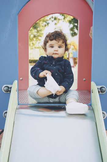 Portrait of cute boy sitting on slide in playground