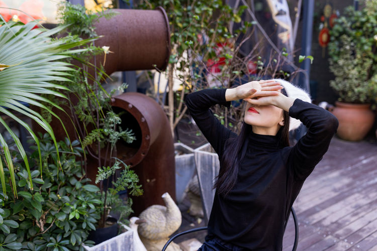 Woman covering eyes sitting on chair by plants