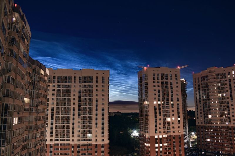 Low angle view of illuminated buildings against noctilucent clouds at night