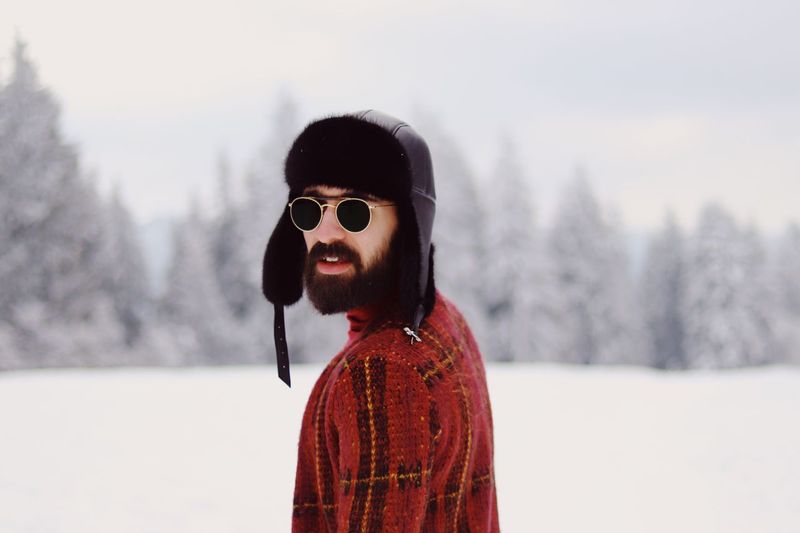 Portrait of young man wearing sunglasses while standing on snow covered filed