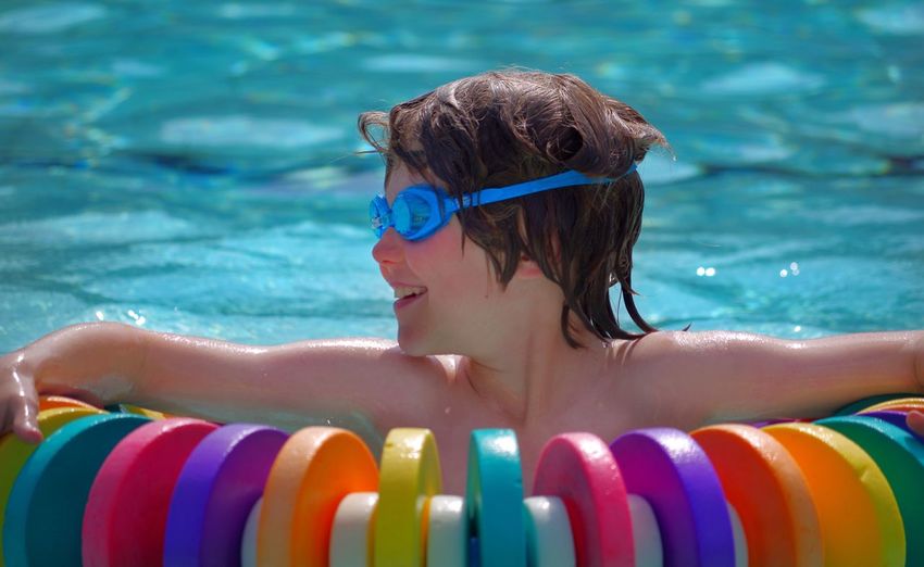 Close-up of child wearing water goggles in pool resting on buoy