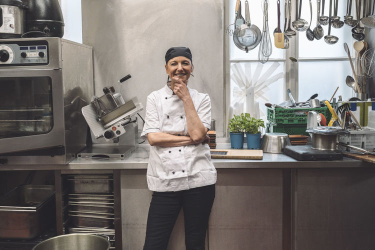 Portrait of happy mature chef with hand on chin in commercial kitchen