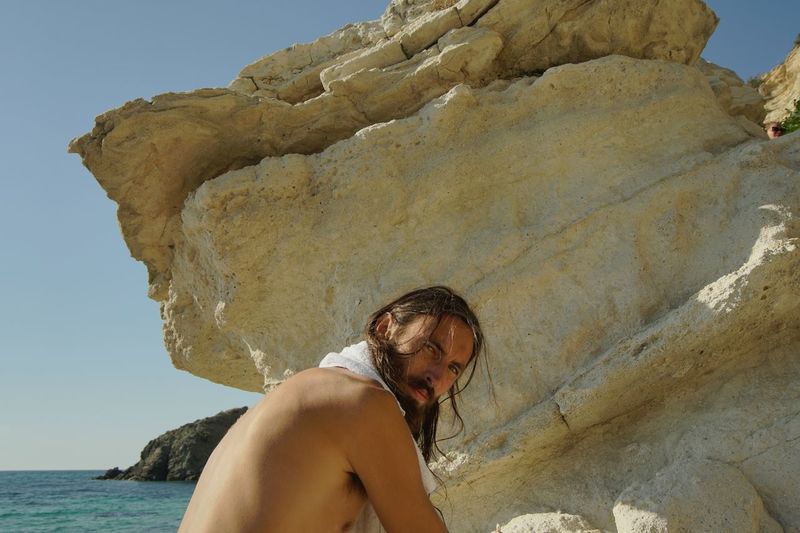 Portrait of shirtless man against rock formation at beach
