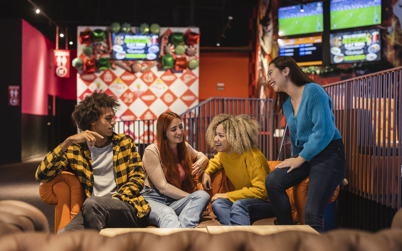 Multiracial friends having fun sitting on sofa at bowling alley