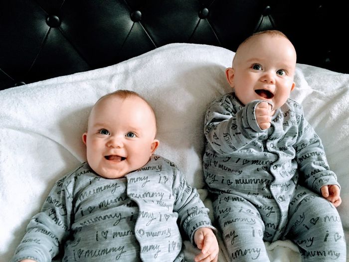Cute twin baby boys lying down on bed at home