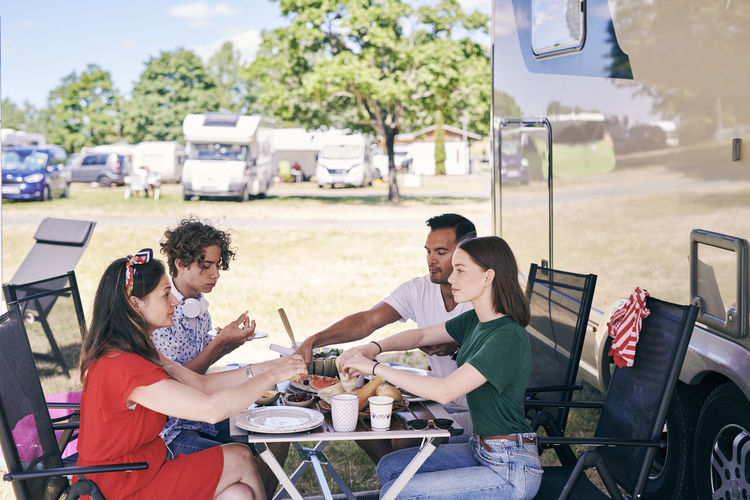 Family enjoying food at table while sitting outside camper van in trailer park