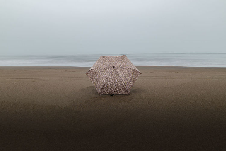 Deck chair on sand at beach against sky
