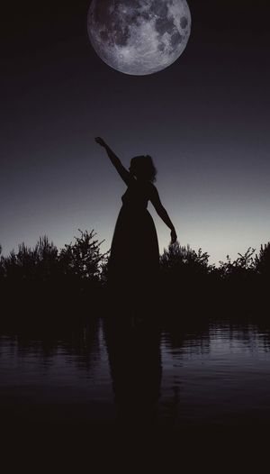 Silhouette woman standing by lake against sky at night