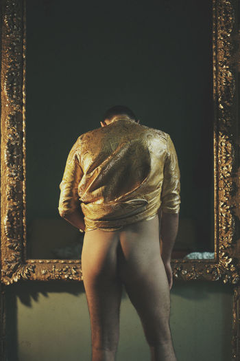Rear view of pant less man standing against picture frame