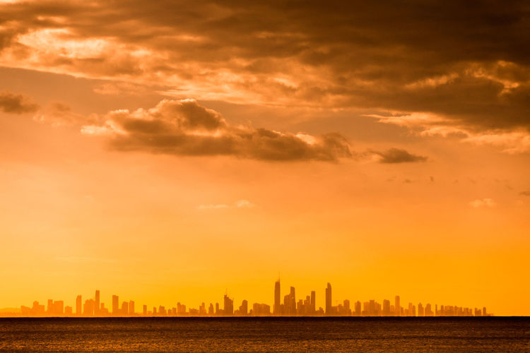 Distant view of city by sea against orange sky