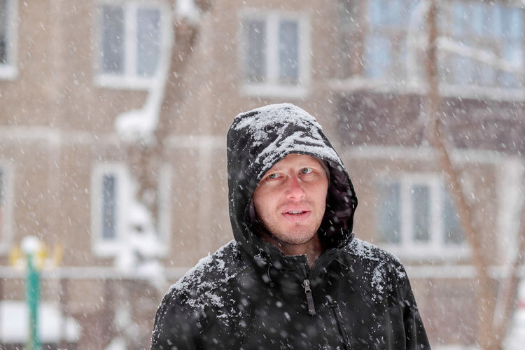 A man in a hood during a snowfall. portrait of a man in winter. serious look