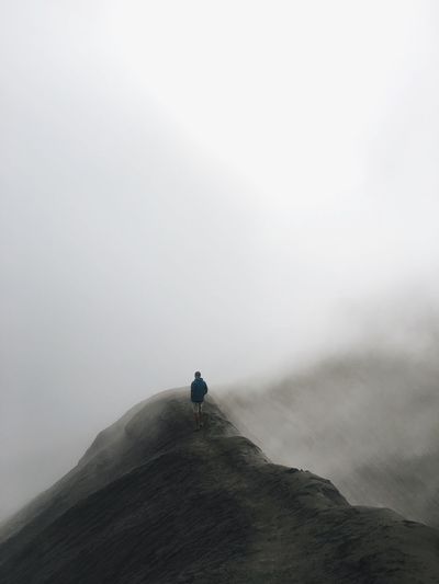 Man standing on mountain against sky during foggy weather