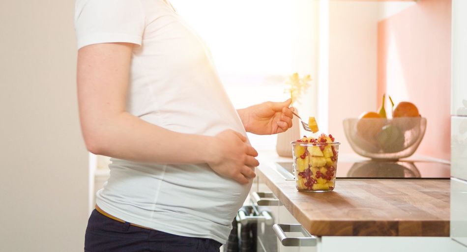 Midsection of pregnant woman standing by fruits on kitchen counter