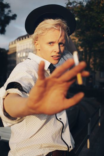 Portrait of woman gesturing while holding cigarette against trees