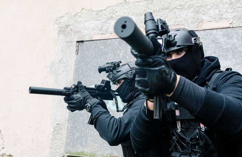 Full body of unrecognizable special forces fighters in battle gear and protective helmets aiming with modern rifles near old building walls