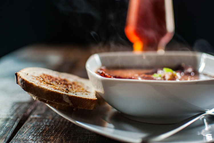 Close-up of soup with bread on wooden table against black background