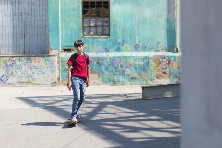 Full length of student skateboarding on road in city during sunny day