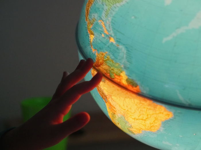 Cropped hand touching illuminated globe in room