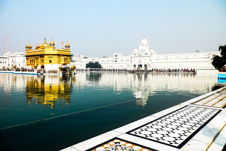 Golden temple by lake against sky
