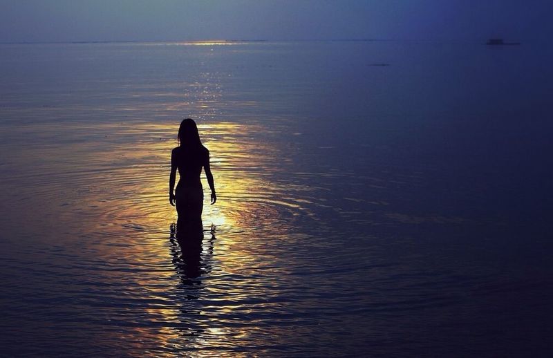 Silhouette of woman in sea at sunset