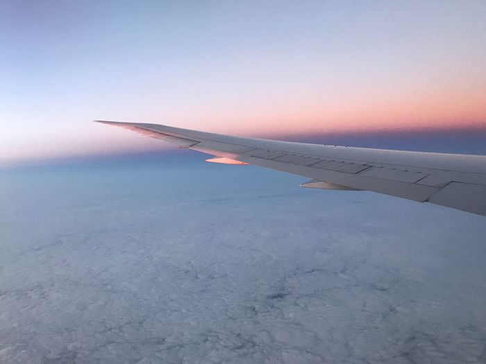 Airplane wing over landscape against sky during sunset