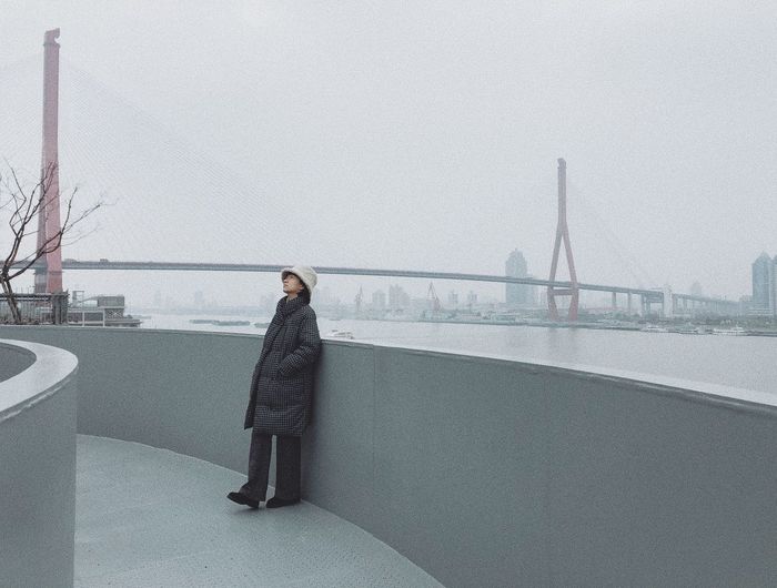 Side view of woman standing on bridge against sky