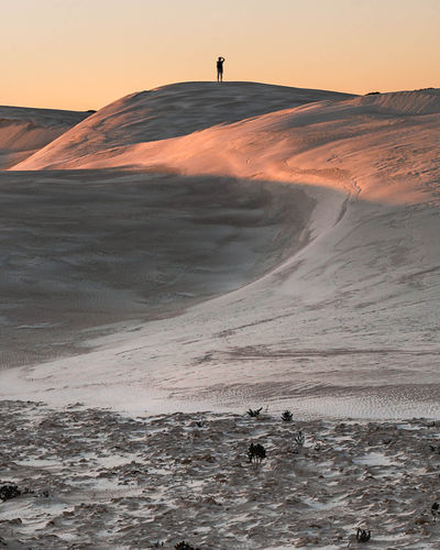 Distant view of man on sand dune in desert against sky