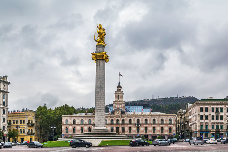 Statue in city against cloudy sky