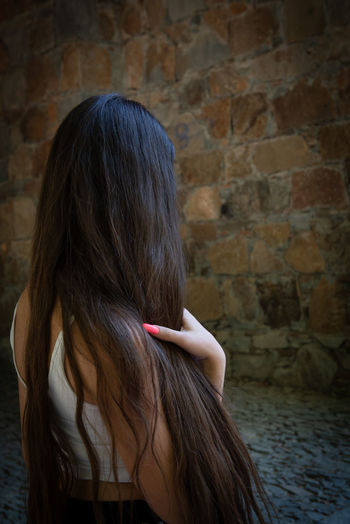 Rear view of woman holding hair standing against wall