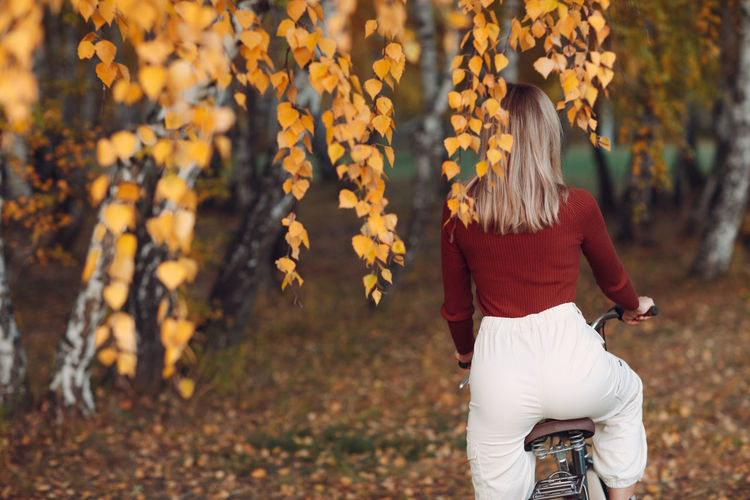 Rear view of woman standing amidst leaves during autumn