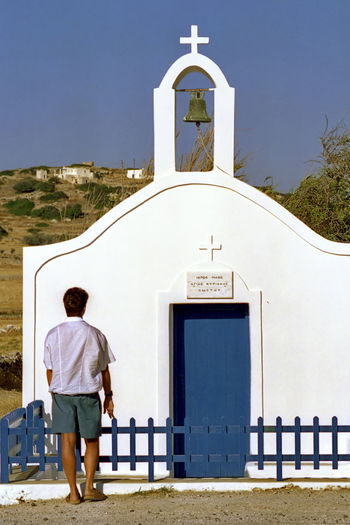 Rear view of man standing by church against sky