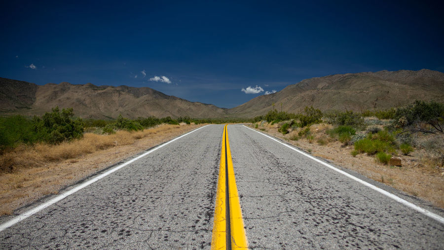 Road leading towards mountains against blue sky