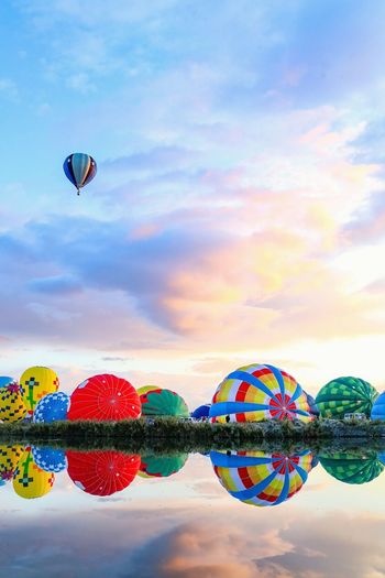 Hot air balloons flying over lake against sky during sunset