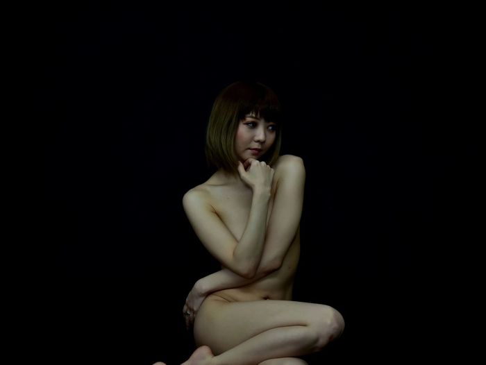 Portrait of woman sitting against black background