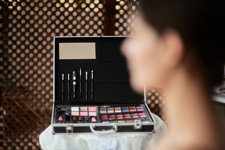 Blurred female model waiting for makeup sitting against opened suitcase with brushes and palettes on table