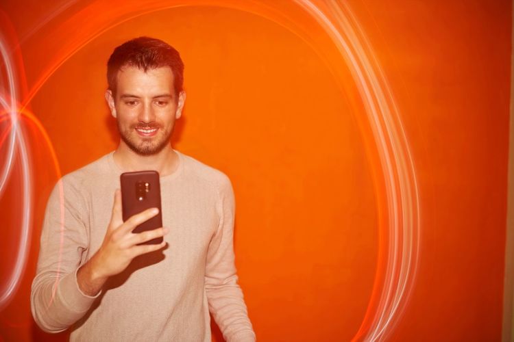 Young man looking the smartphone on a orange colored background