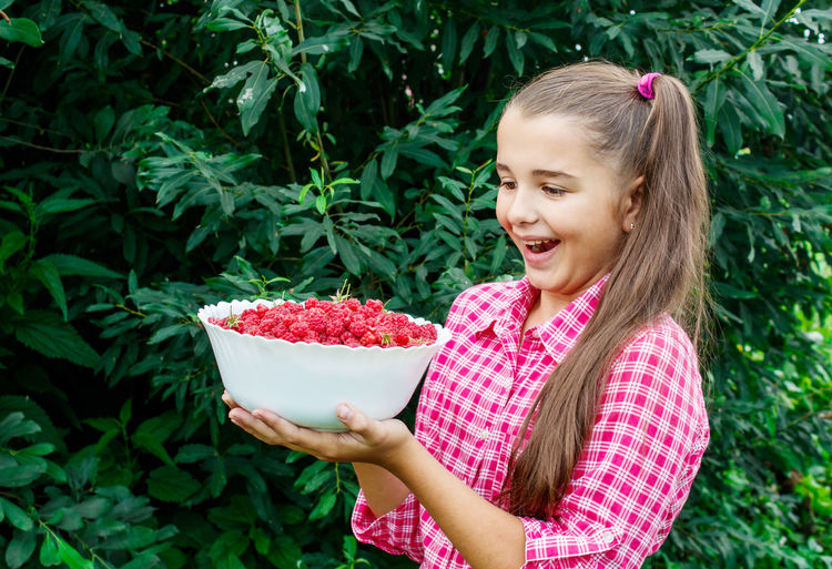 Girl holding raspberries in bowl against plants